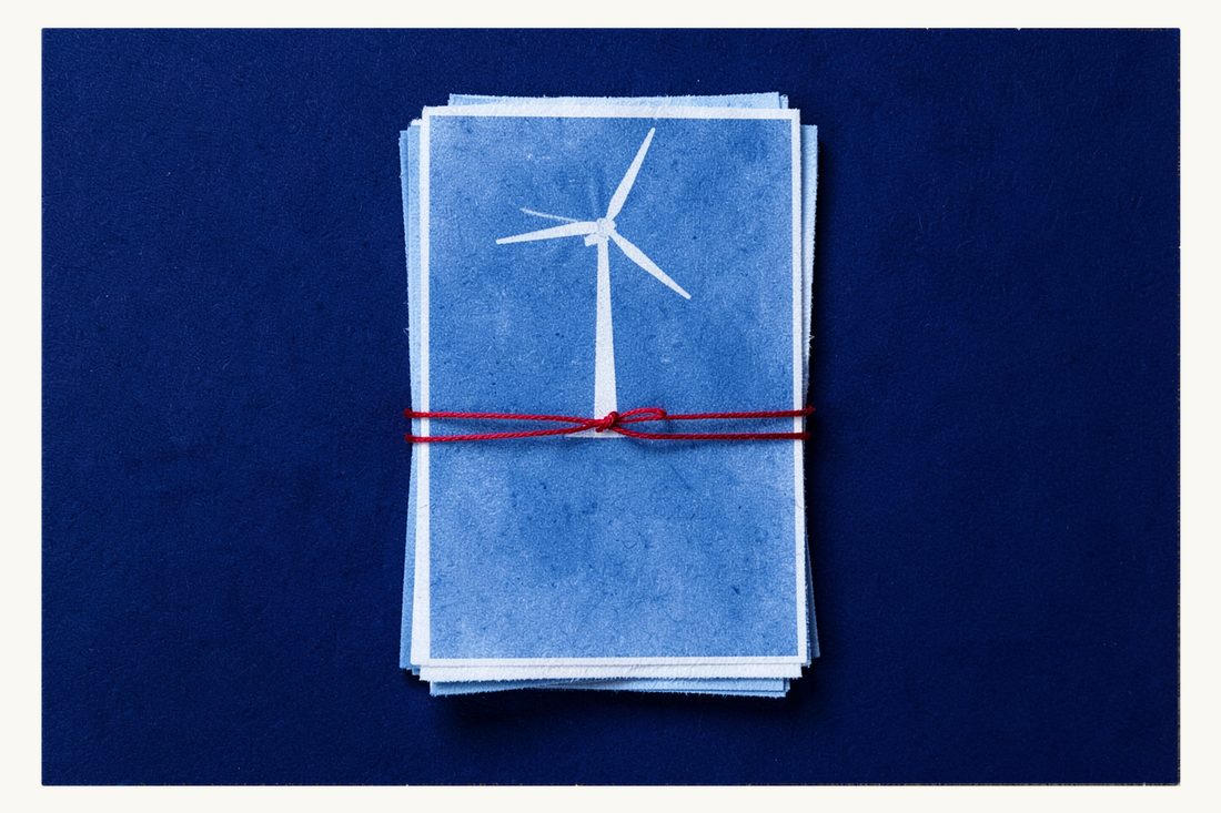 Permits and approvals for a renewable energy project: a tall pile of blank sheets bound by a red thread with a wind turbine standing on top, cyanotype print