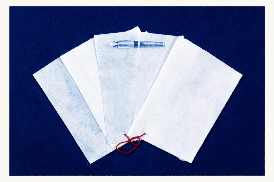 Commercial contracts drafted and reviewed: a wide fan of blank sheets bound at the base by a red thread, a fountain pen on top, cyanotype print