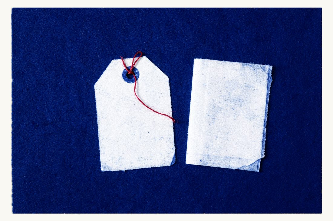 Trademark registration before TÜRKPATENT: a large blank product swing tag tied through its eyelet with the red thread to a closed document folder, cyanotype print